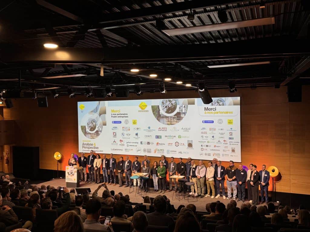 Intervenants et partenaires alignés sur scène devant l’écran de remerciements, salle comble