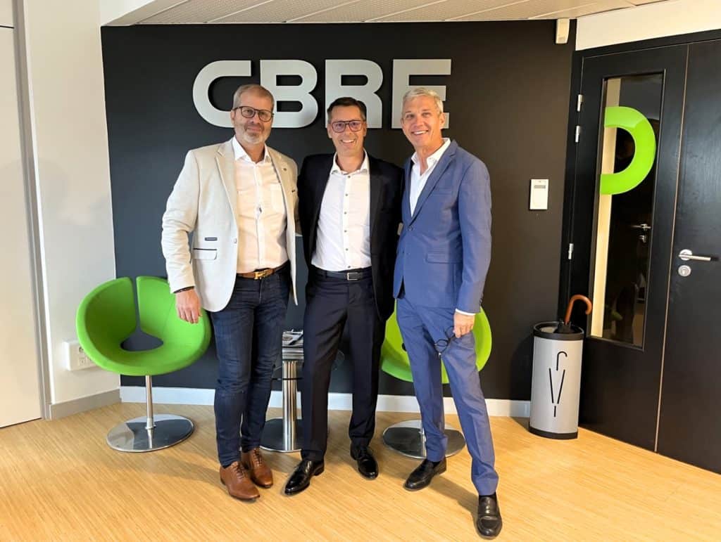 Trois hommes en veste posant devant le logo CBRE, dans l’agence de Grenoble