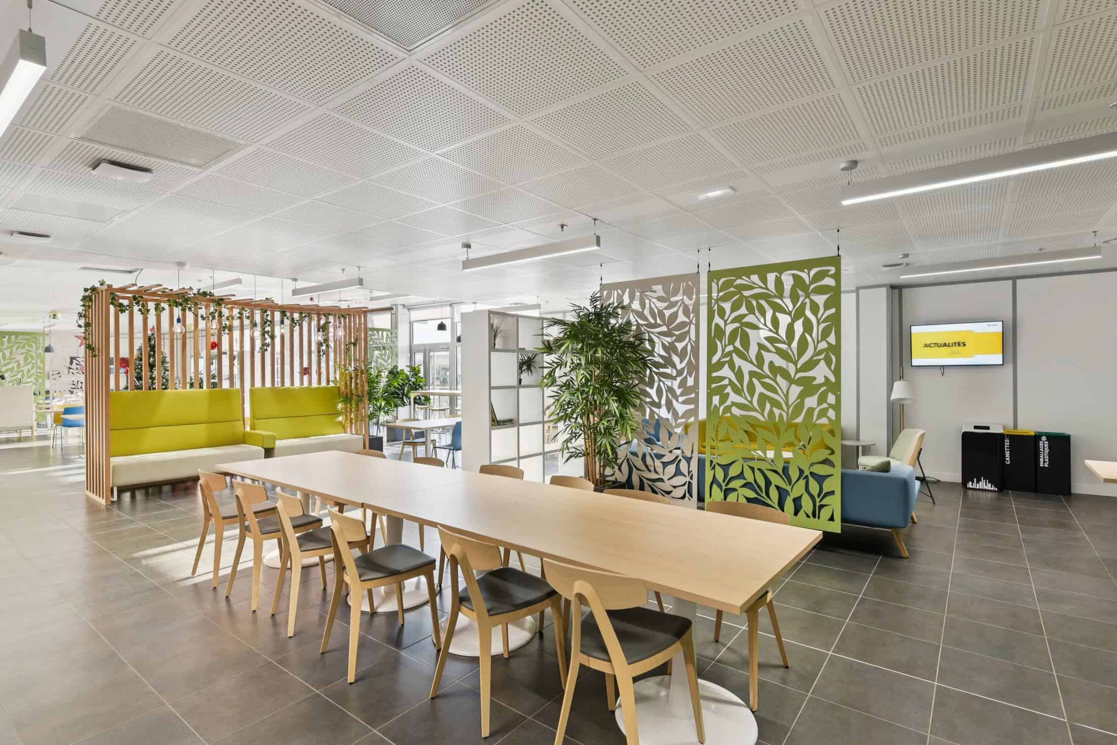 Espace de convivialité meublé par WOM chez Stryker, en Isère : table en bois clair, banquettes vertes et claustras
