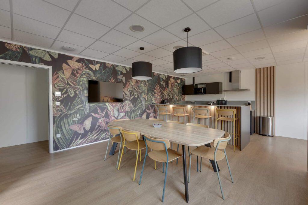 Espace de restauration de Care TP à L’Albenc, équipé par WOM : grande table en bois et papier peint végétal